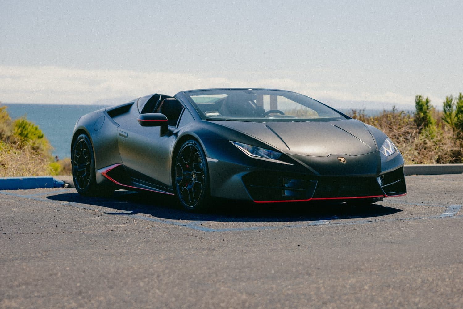 Matte-black Lamborghini Huracán EVO Spyder, front three-quarter above the Orange County coast